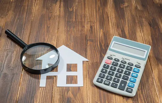 A calculator and magnifying glass sitting on top of a wooden table.